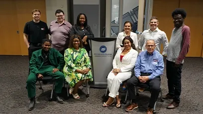 Eleven attendees of the small business networking event pose together for a group photo in front of a Rio Salado College podium. They are dressed in a mix of business and casual attire, smiling warmly at the camera in a spacious event room with wood-paneled doors in the background.