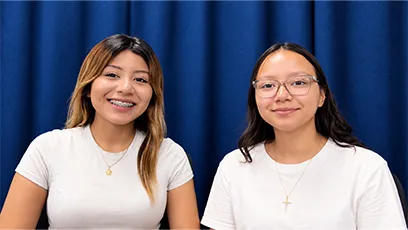 Allyson Hurtado Fernandez, left, and Silvana Castro Aguilar, right, smile at the camera while seated together in front of a blue curtain.