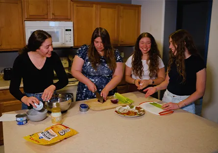 Alexandria Woodruff stands with her three sisters in a kitchen, smiling and preparing food together at a countertop.