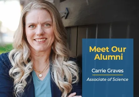 Carrie Graves, a blonde woman with long wavy hair, smiles while standing outdoors next to a dark wooden wall. She is wearing a navy blazer over a light blue top and layered necklaces. A blue graphic box on the right reads: ‘Meet Our Alumni — Carrie Graves, Associate of Science.’