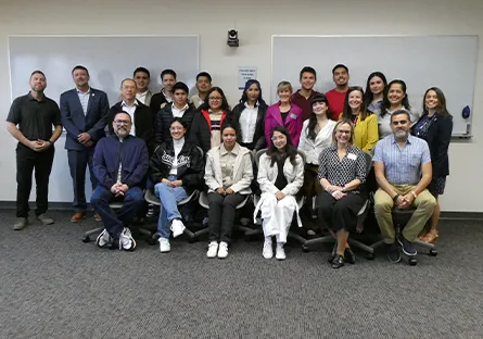 Group photo of students and instructors gathered in a classroom, standing and seated in rows.