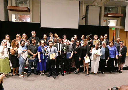 Large group of students and faculty pose together on stage holding certificates during an induction ceremony.