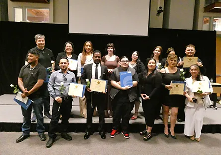 Inductees stand together on stage holding certificates and folders during a recognition ceremony.