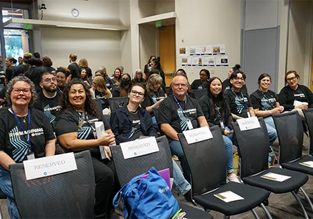 A group of attendees seated in a conference room, smiling toward the camera, with “Reserved” signs placed on several chairs.