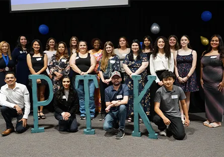 Large group of newly inducted Phi Theta Kappa members posing together on stage behind large “PTK” letters during the 2026 induction ceremony.