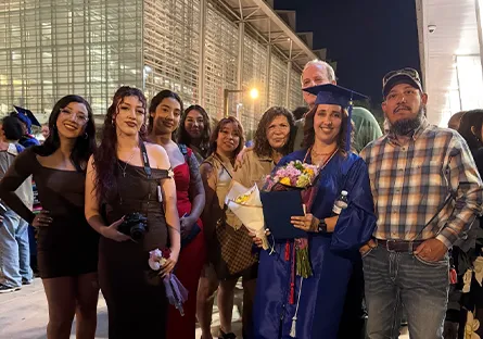 Rio Salado College graduate Diana Loya, wearing a blue cap and gown and holding flowers and her diploma cover, poses with seven family members outside the commencement venue at night.