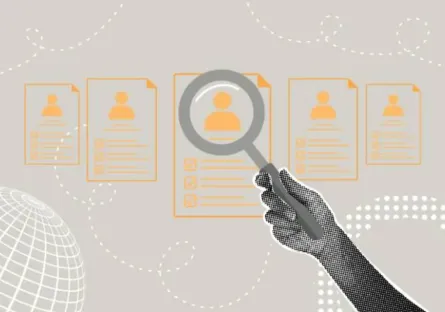 A hand holding a magnifying glass over a lineup of resumes